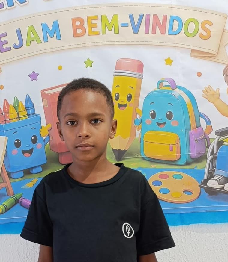 Aluno do projeto diante do painel de boas-vindas da sala de reforço