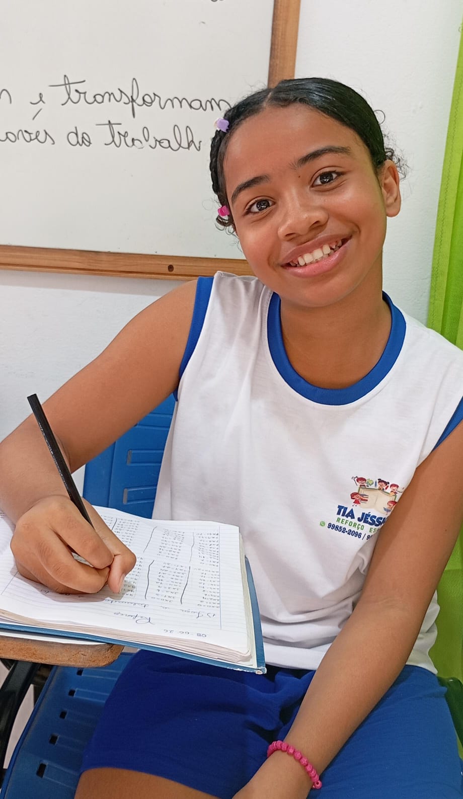 Aluna do projeto sorrindo enquanto escreve no caderno durante o reforço