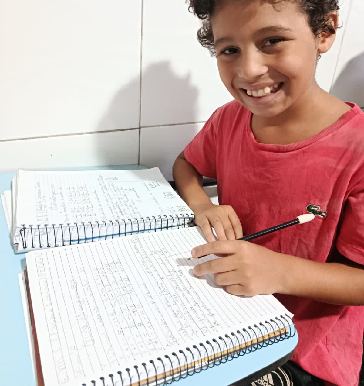 Aluno do projeto sorrindo com os cadernos de exercícios abertos
