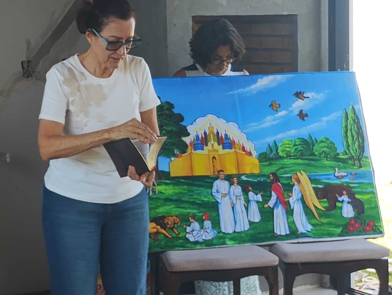 Professora voluntária lendo a Bíblia para as crianças diante de um quadro pintado