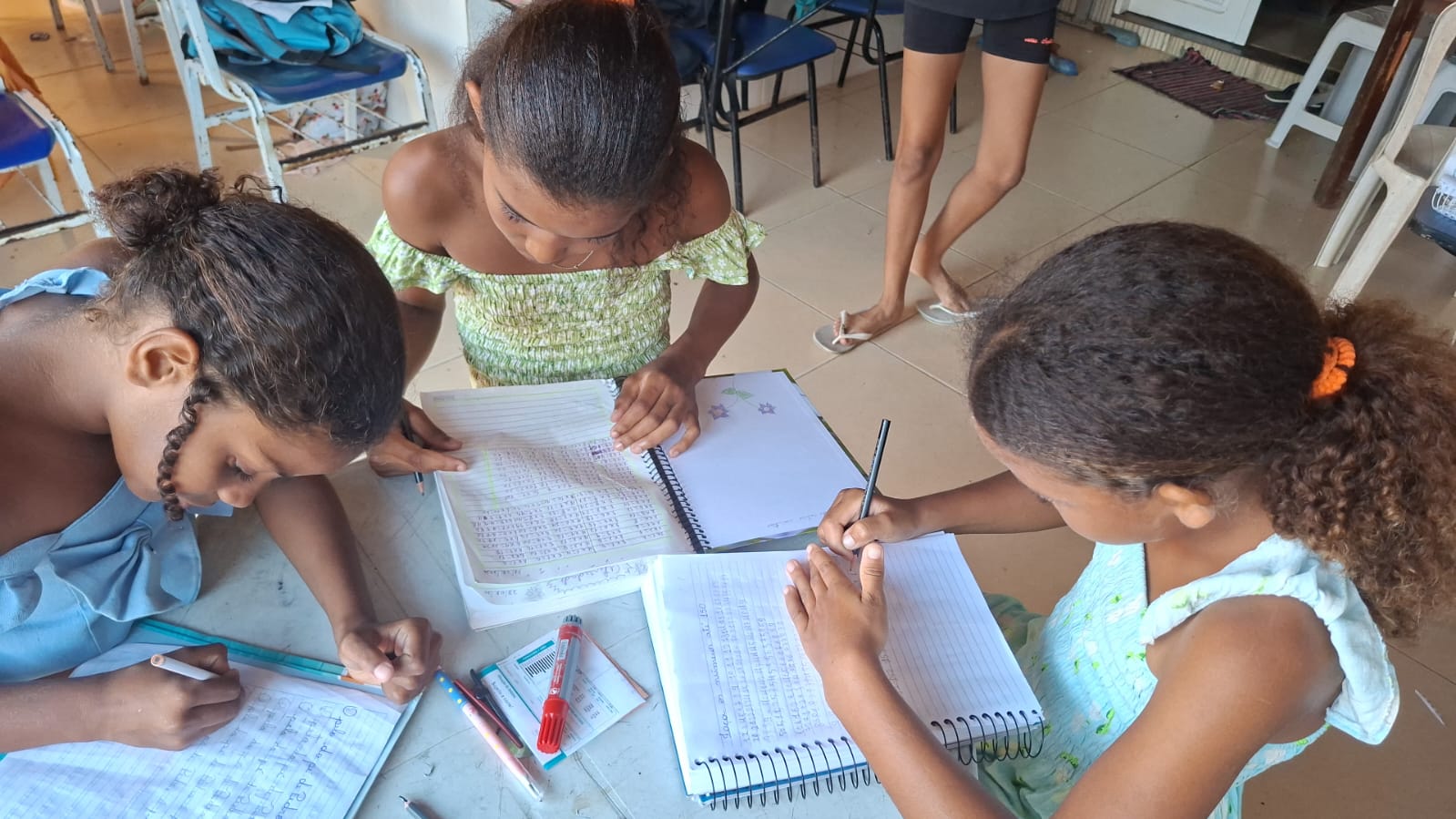 Três alunas do projeto escrevendo nos cadernos durante a aula de reforço