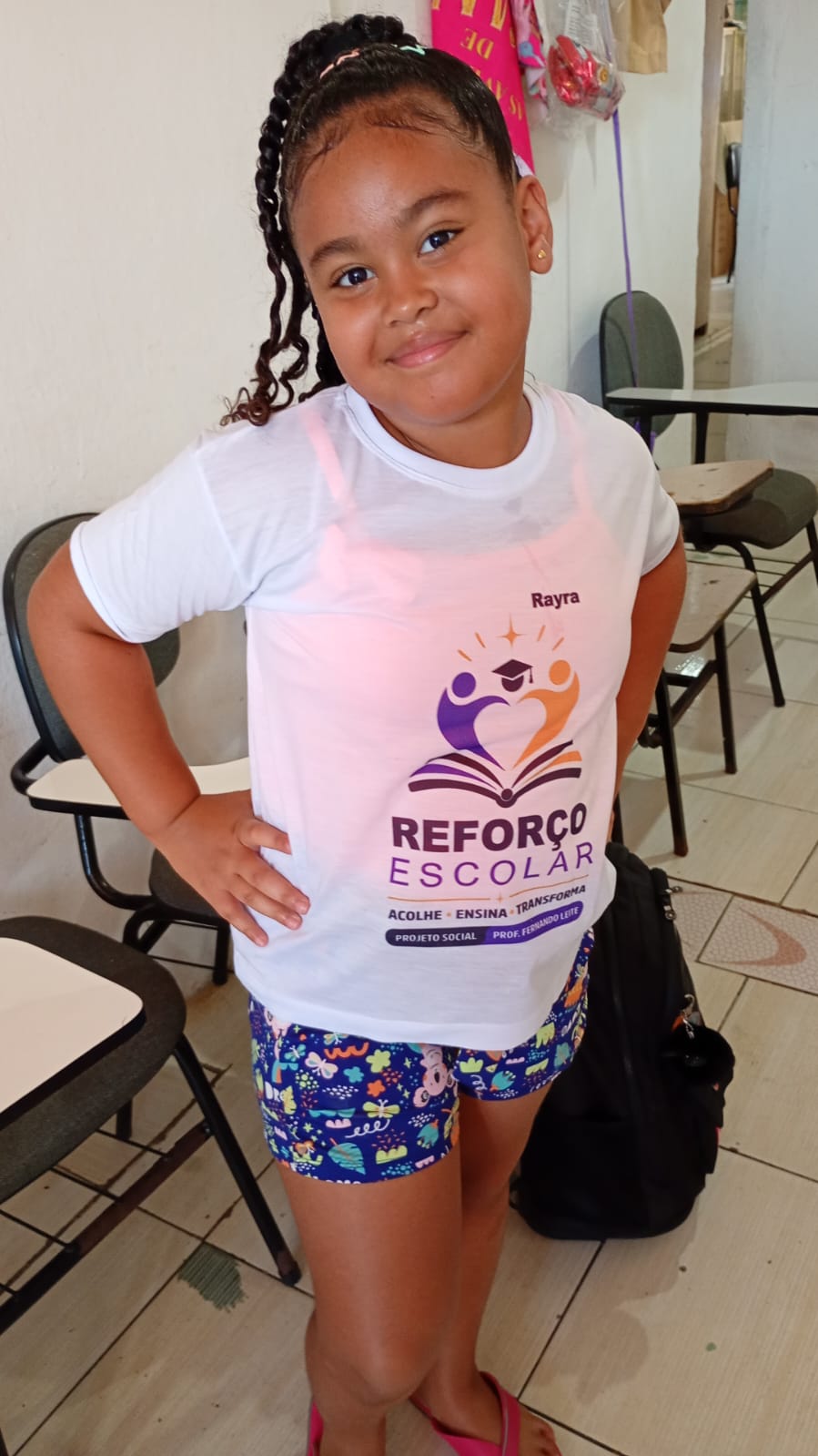 Aluna com a camiseta do reforço escolar posando na sala de aula