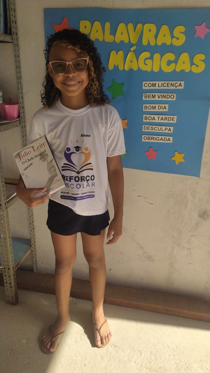 Aluna do projeto com um livro, diante do painel das palavras mágicas