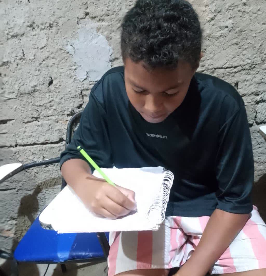 Aluno do projeto escrevendo no caderno espiral com lápis