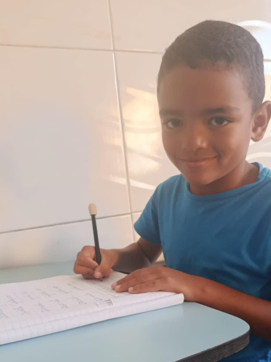 Aluno do projeto escrevendo o exercício no caderno de caligrafia