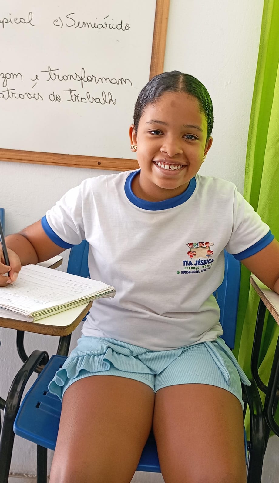 Aluna do projeto sorrindo enquanto faz a atividade no caderno