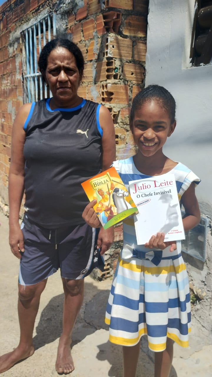 Aluna do projeto ao lado da avó, com os livros recebidos no reforço escolar